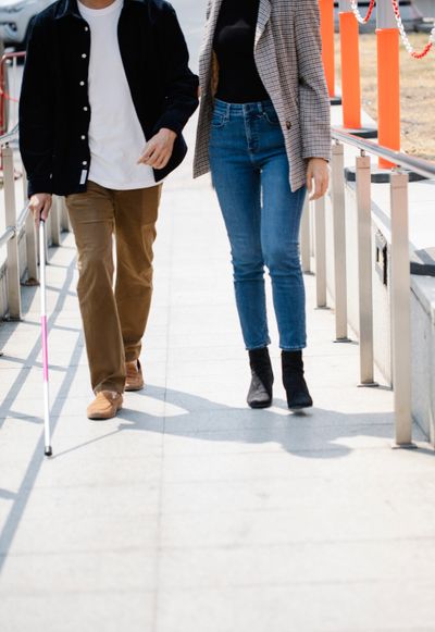 Two people walking together, one guiding the other who uses a white cane — photo by Eren Li on Pexels