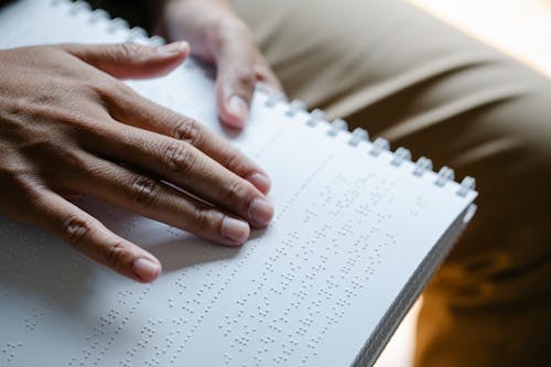 Closeup of crop unrecognizable blind person touching page with braille text while reading special book