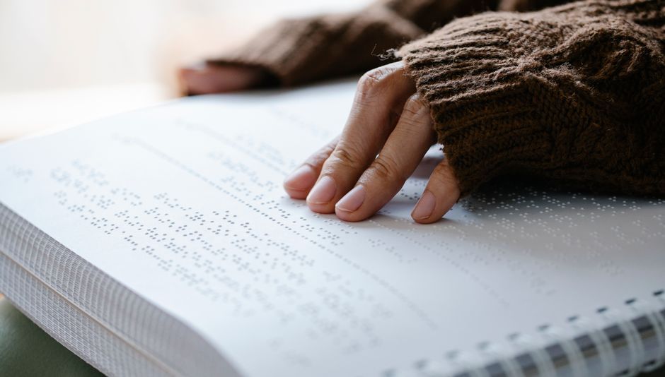 A person's hand in knitted sweater reading braille text on paper.