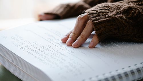 Free A person's hand in knitted sweater reading braille text on paper. Stock Photo