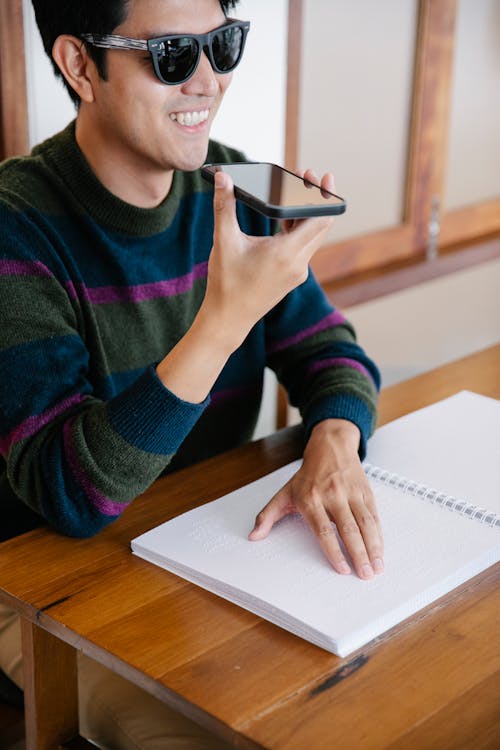 Photo of Man Talking to the Phone while Studying Using Braille 