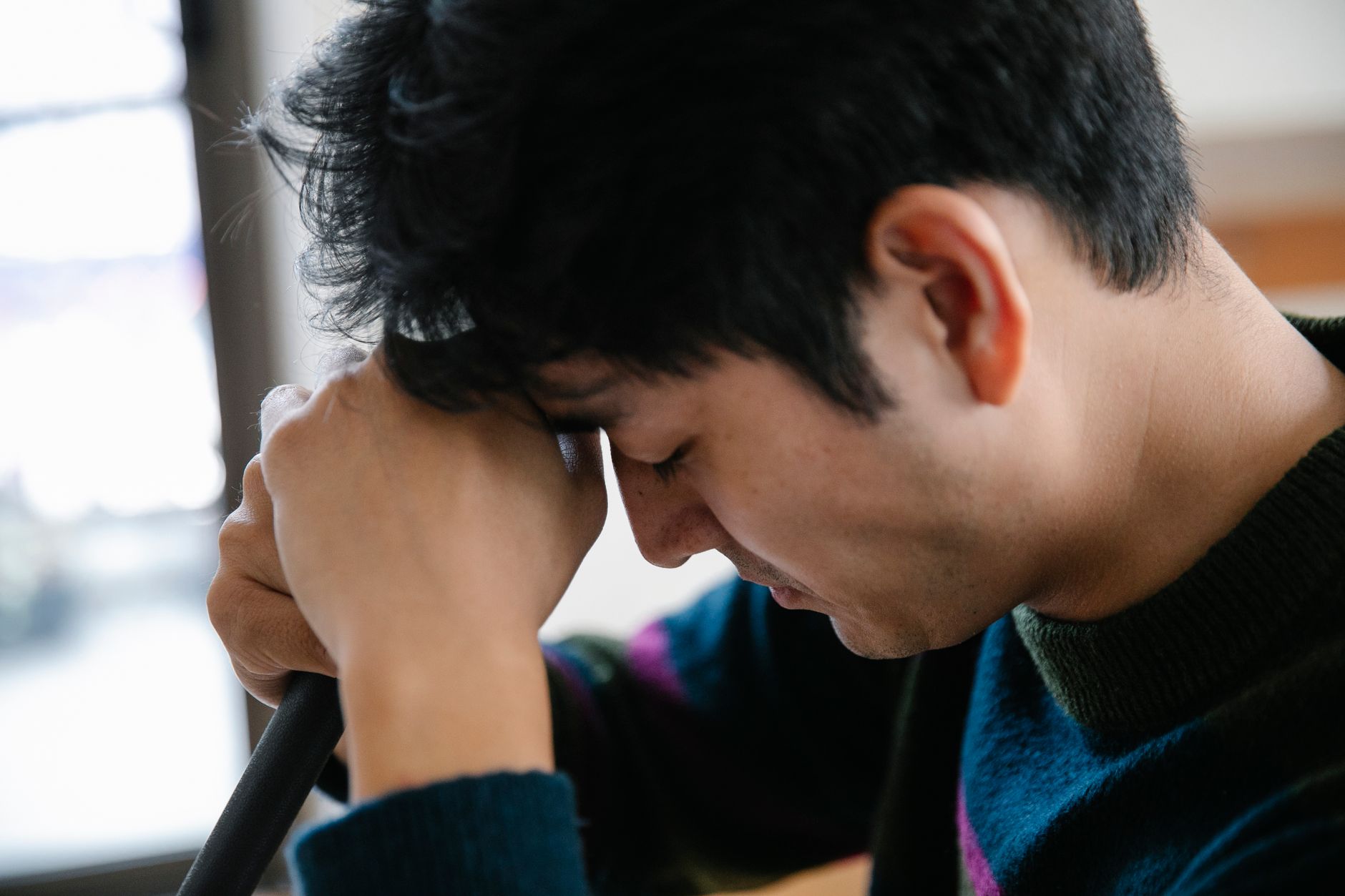 Close-up of a man looking stressed as he rests his head on his arms indoors.