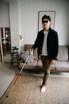 A man wearing sunglasses uses a walking stick for guidance indoors, reflecting independence and style.