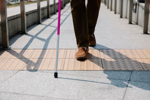 Close-up of a person using a walking cane on tactile pavement outdoors.