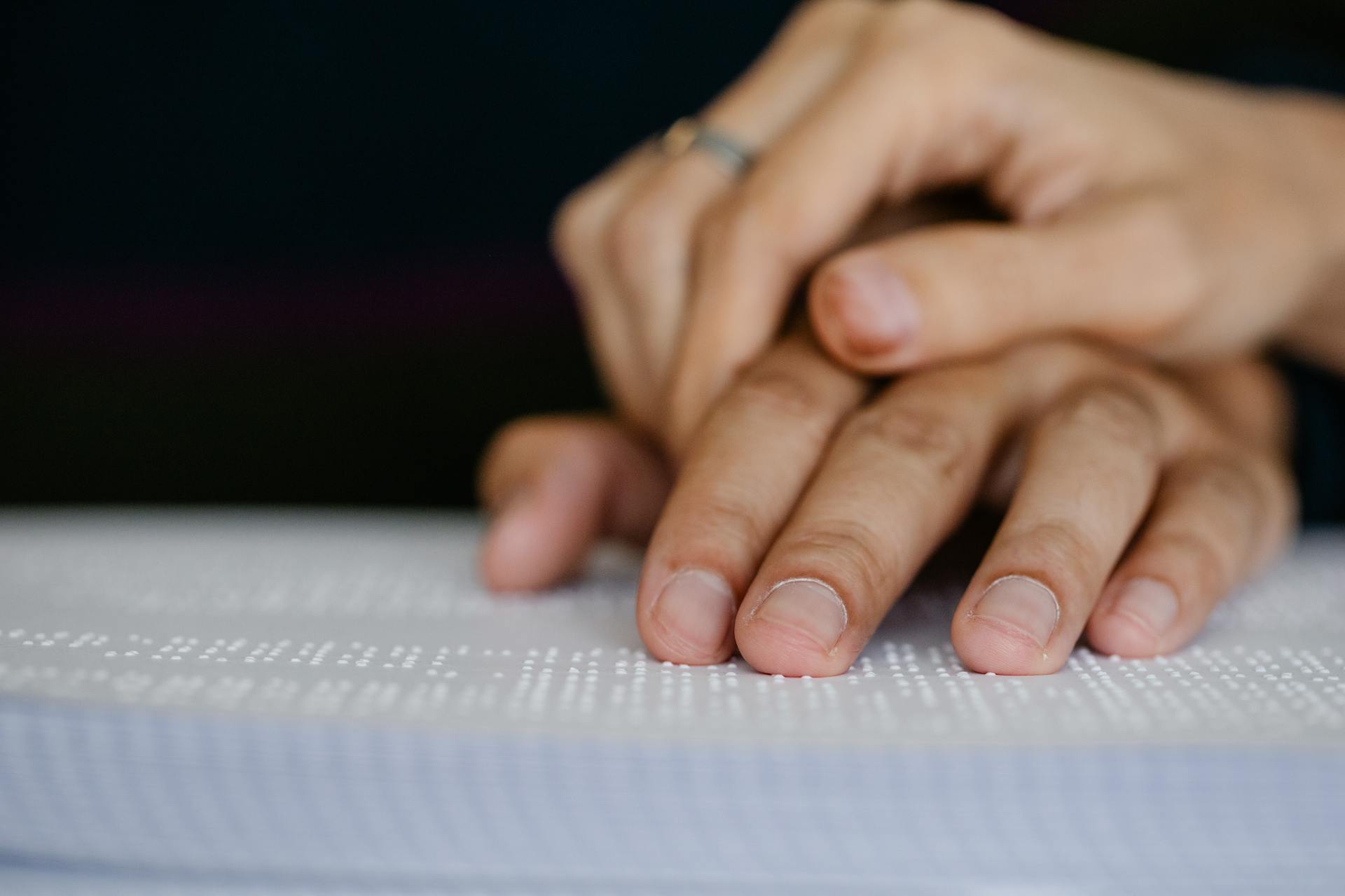 A detailed shot of hands touching a Braille book, symbolizing accessibility and visual impairment.