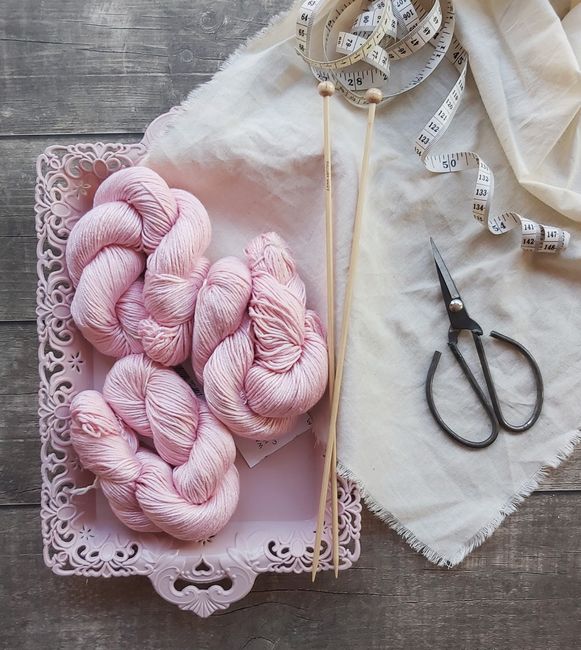 A flat lay of pink yarn, scissors, knitting needles, and textile on a vintage tray.