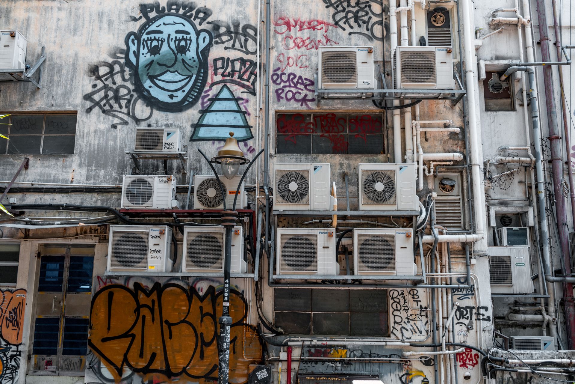 A city wall covered in graffiti with multiple air conditioning units mounted.