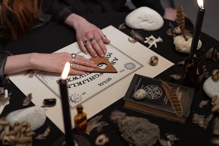 Hands Of Women On A Ouija Board Near Burning Candles