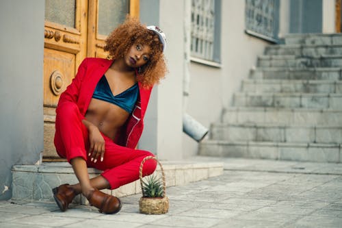 Free Woman Wearing Red Coat and Pants Sitting Outside Gray Building Stock Photo