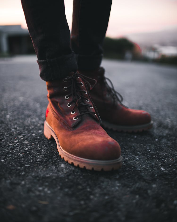 Person Wearing Pair Of Brown Timberland Work Boots And Black Denim Skinny Jeans Standing On Asphalt Road