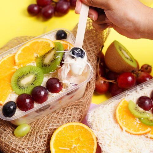 Free Vibrant close-up of a tropical fruit salad featuring fresh oranges, kiwi, and grapes in a dessert container. Stock Photo