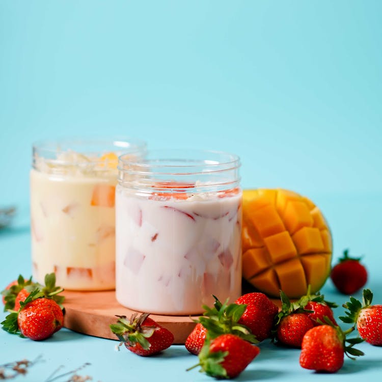 Cut Strawberries In Yoghurt In Plastic Jars Beside Strawberries On Blue Table