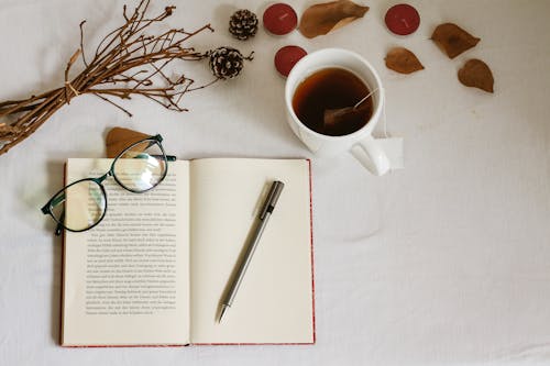Notebook, Eyeglasses, Cup of Tea, Candles and Leaves on White Table