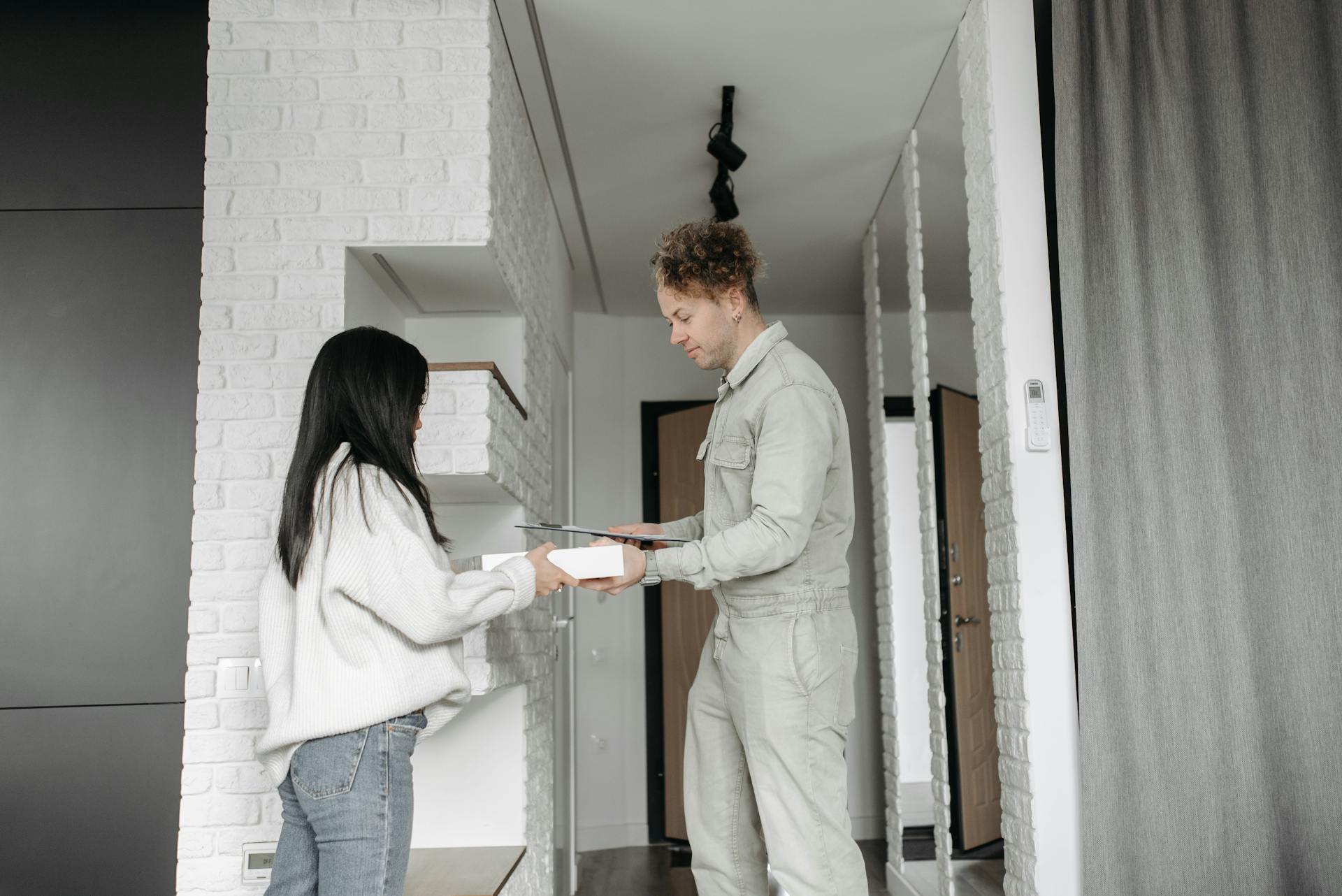 A woman receives a package from a delivery man in a modern home setting, highlighting convenience and online shopping.