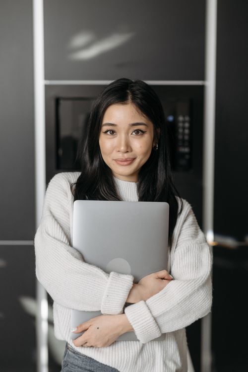 Free Asian woman smiling and embracing laptop inside a modern home setting. Stock Photo