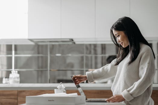 Smiling woman unpacks a laptop in an elegant kitchen, showcasing comfort and technology.