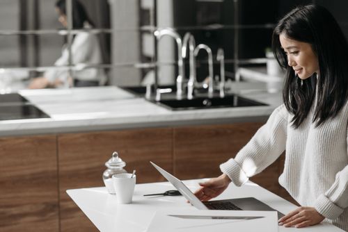 Free Asian woman in modern kitchen working on laptop, showcasing productivity and lifestyle. Stock Photo