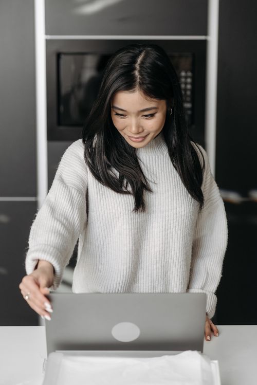 Free Smiling woman in knitted sweater opening laptop in a cozy indoor setting. Stock Photo