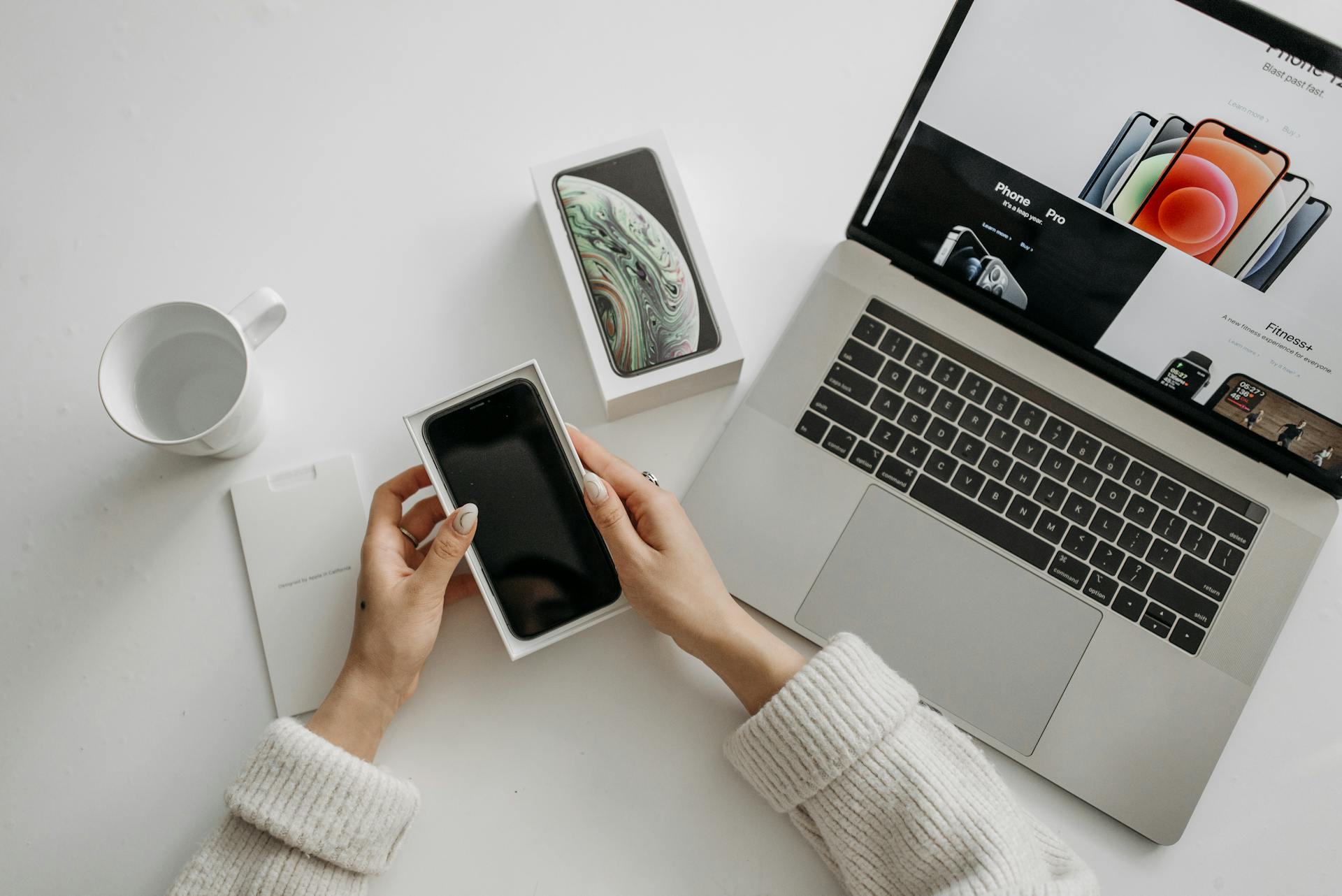 A Person Holding Mobile Phone in the Box with Laptop on the Side