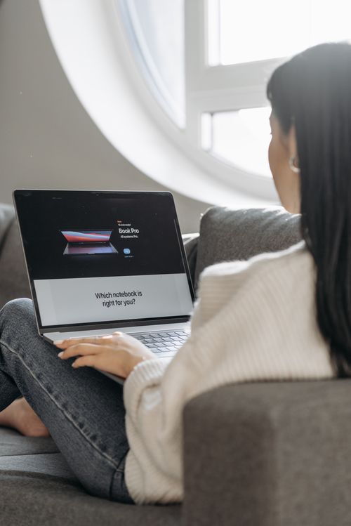 Free Woman sitting on a couch, using laptop under soft daylight. Stock Photo