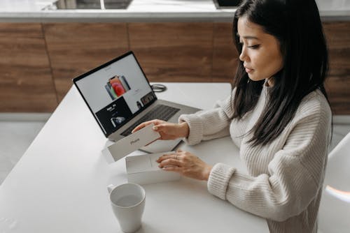 Woman in White Knit Sweater Holding White Box beside Laptop