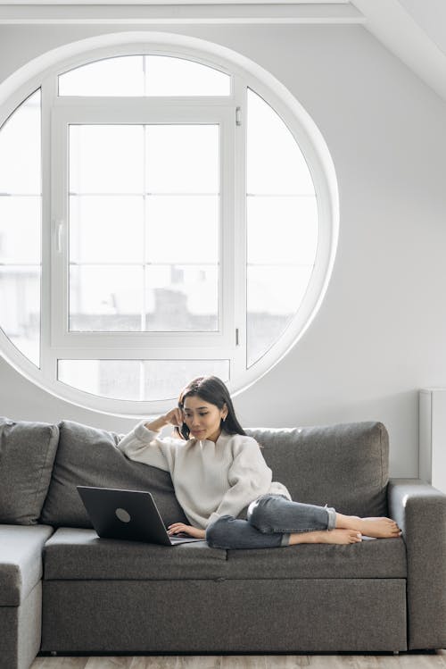 Free A Woman Sitting on the Couch while Using Her Laptop Stock Photo