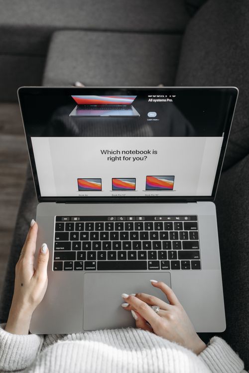 Free Top view of a person using a laptop on a gray couch, browsing different notebook options. Stock Photo