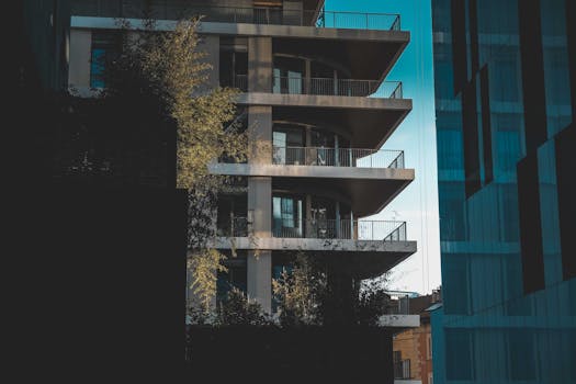 Contemporary residential multistory house with balconies and metal fences located on street with tree and shadow in city against blue sky
