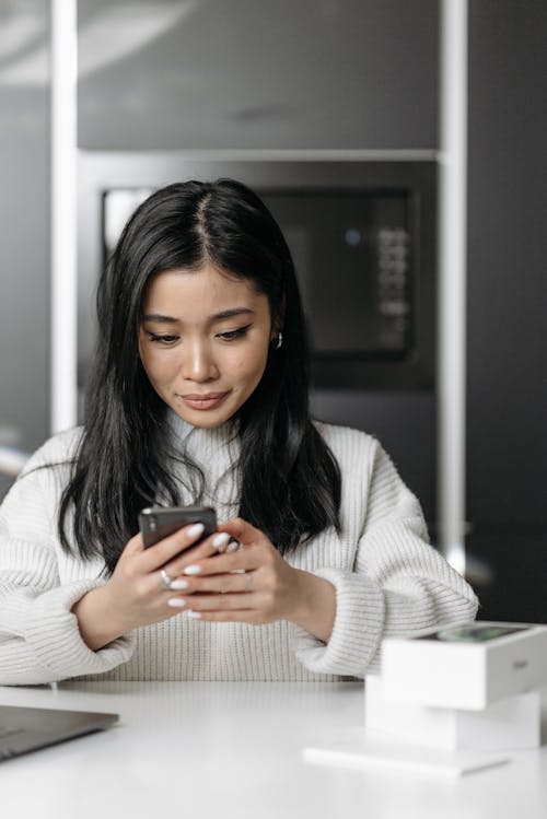 Free Woman in White Sweater Holding a Mobile Phone Stock Photo