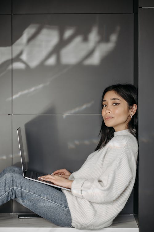 A Woman in White Knitted Sweater Sitting while Using Her Laptop