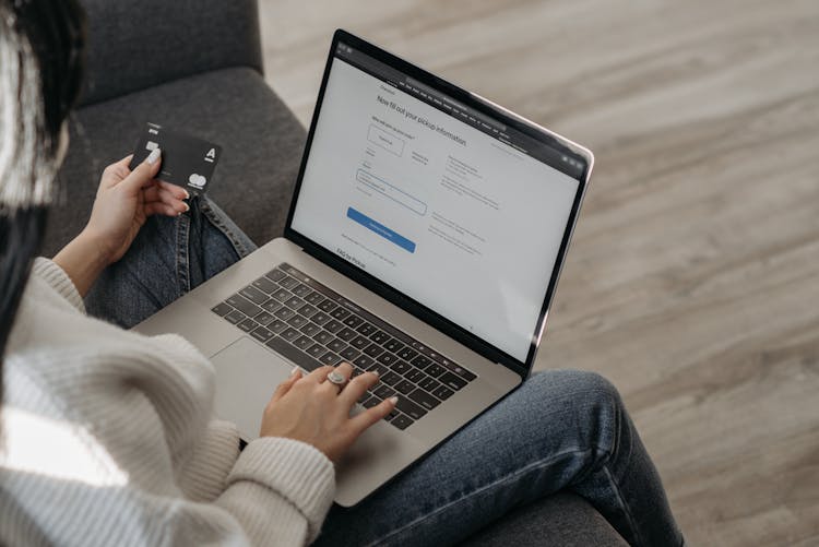 A Person Using Her Laptop While Holding A Credit Card