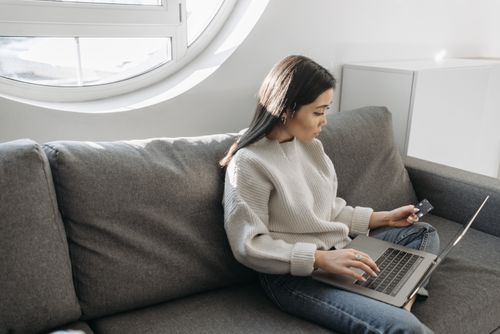 Free Woman sitting on a sofa using a laptop for online shopping indoors, holding a credit card. Stock Photo