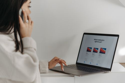Free Asian woman on phone using laptop for online shopping against a white wall. Stock Photo