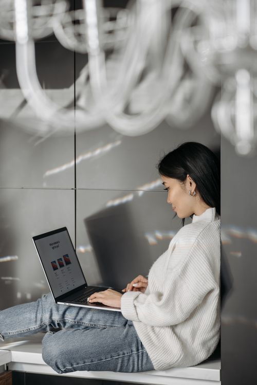 Free Young Asian woman focused on work using a laptop indoors, relaxed and engaged. Stock Photo
