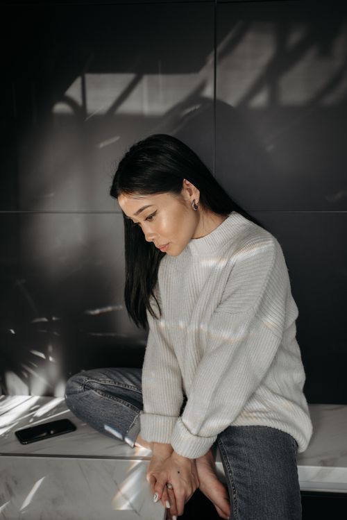 Free Asian woman sits in a contemplative pose indoors wearing casual clothing, mood lighting. Stock Photo