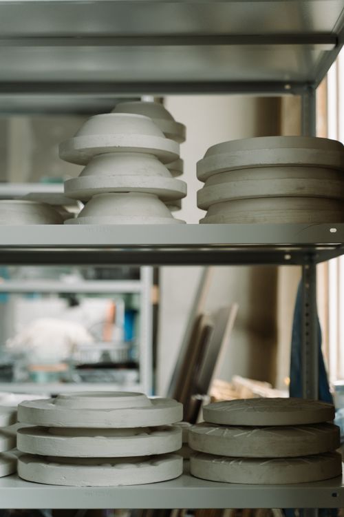 Stacked ceramic plates drying on metal shelves in a workshop