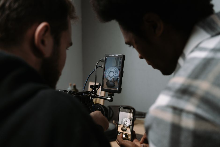 Two men use cameras and smartphones to capture a close-up video in a studio setting.