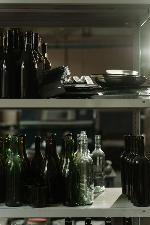 Free A collection of glass bottles on metal shelving in a dimly lit indoor setting, emphasizing recycling and reuse. Stock Photo