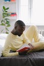 Man in Yellow Long Sleeves Reading Book in the Bed
