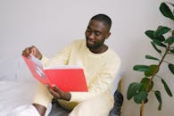 Man Reading a Book while Sitting on the Bed