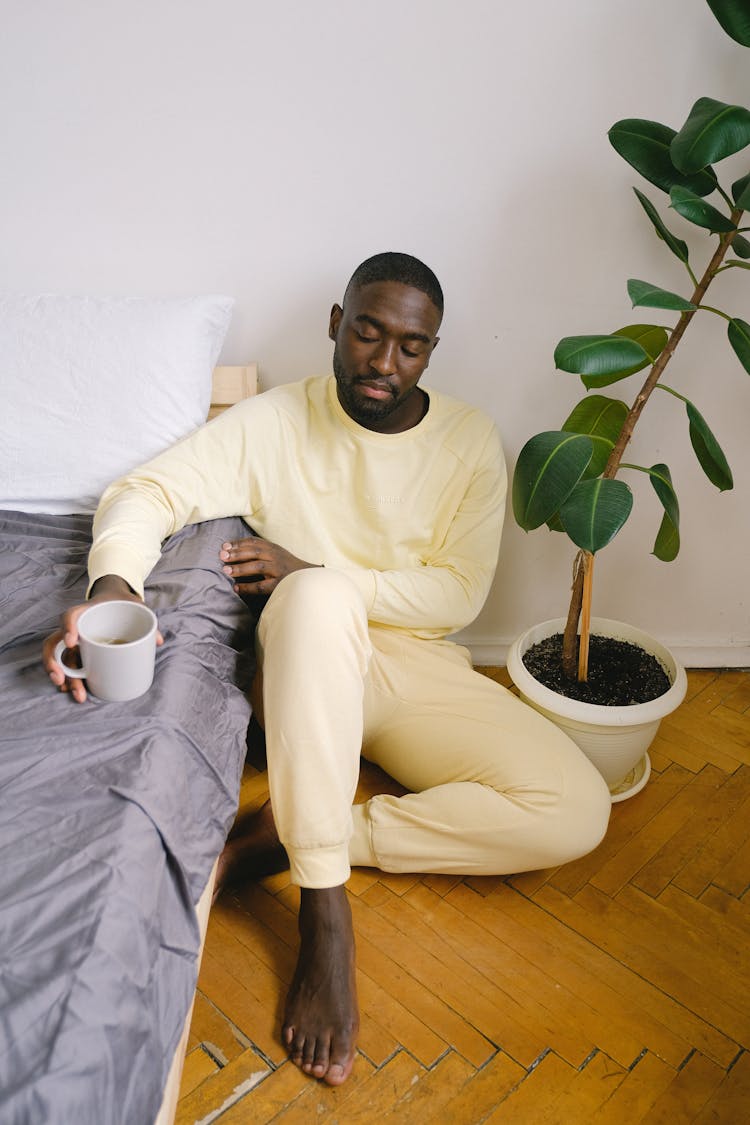 Upset Black Man With Mug Of Coffee In Bedroom