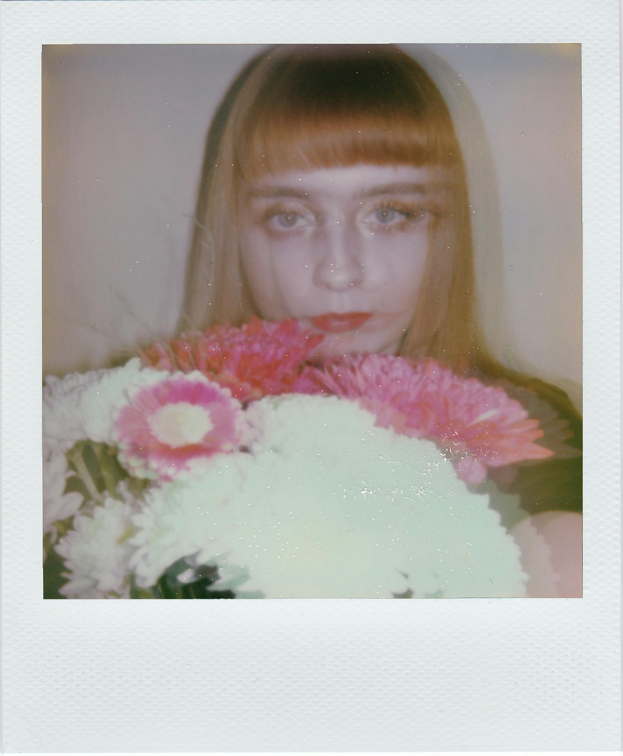 Artistic portrait of a young woman holding a vibrant floral bouquet with a blurred effect.