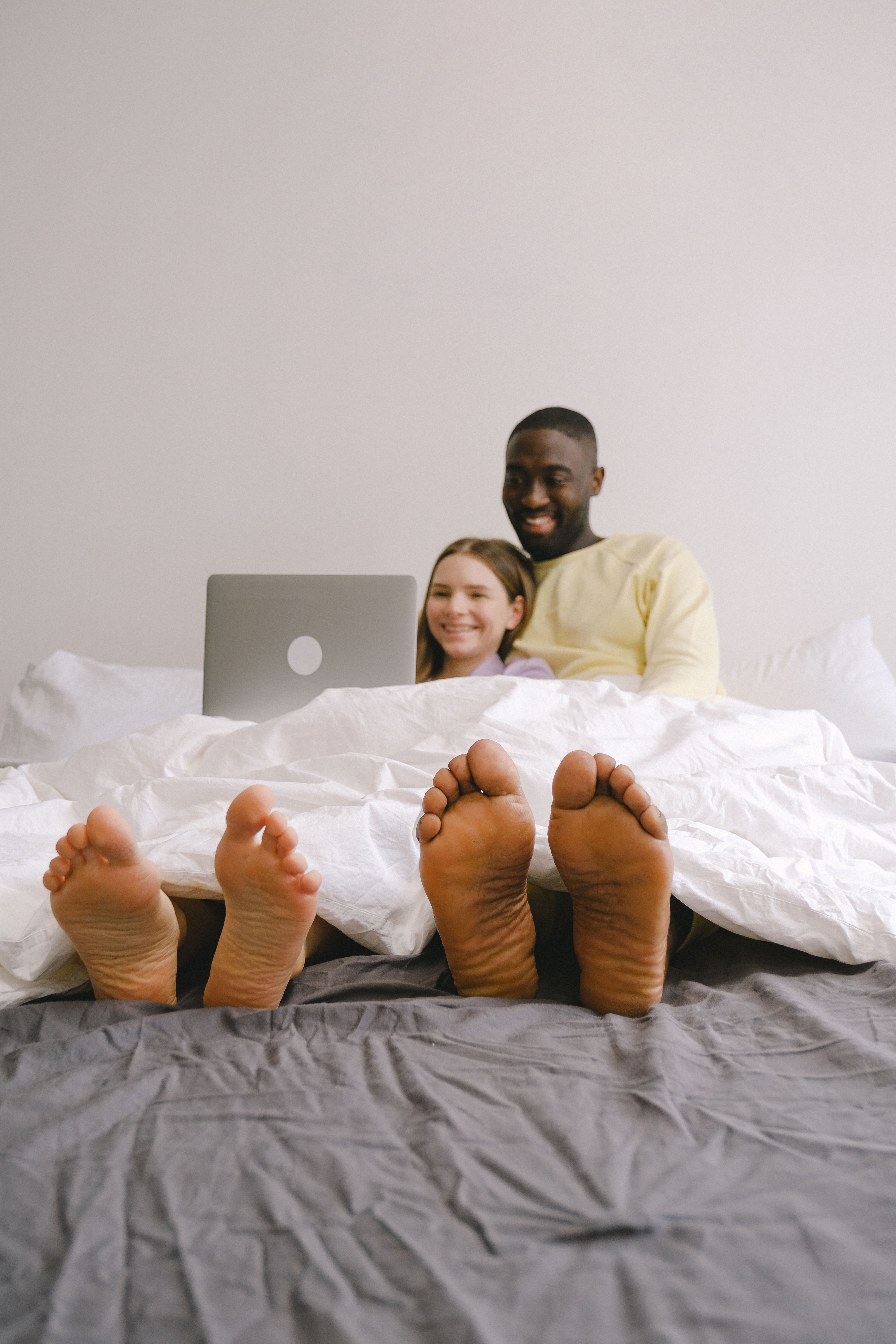Happy interracial couple bonding while watching something on a laptop in bed.