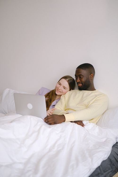 Free Smiling couple using a laptop in bed, enjoying a cozy moment indoors. Stock Photo
