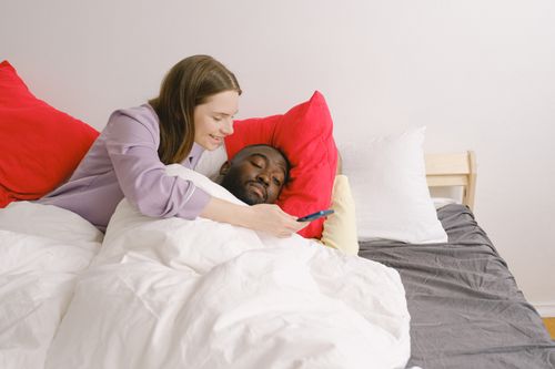 Free Interracial couple enjoying a relaxing morning in bed, sharing a moment with a mobile phone. Stock Photo