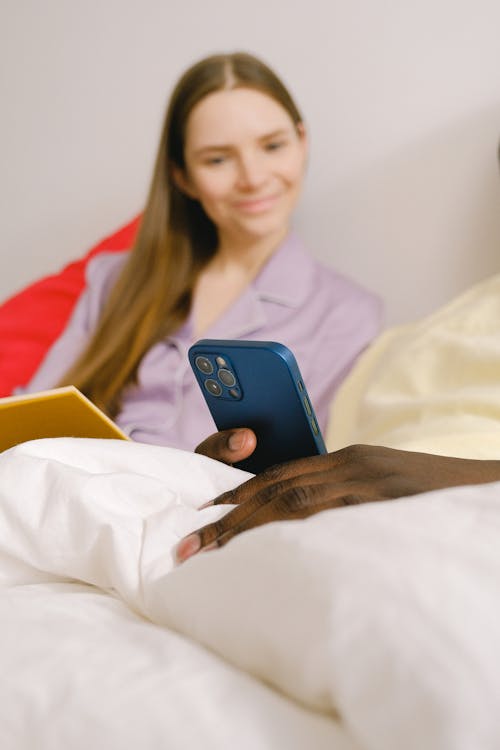 Cheerful woman near crop black man with smartphone on bed