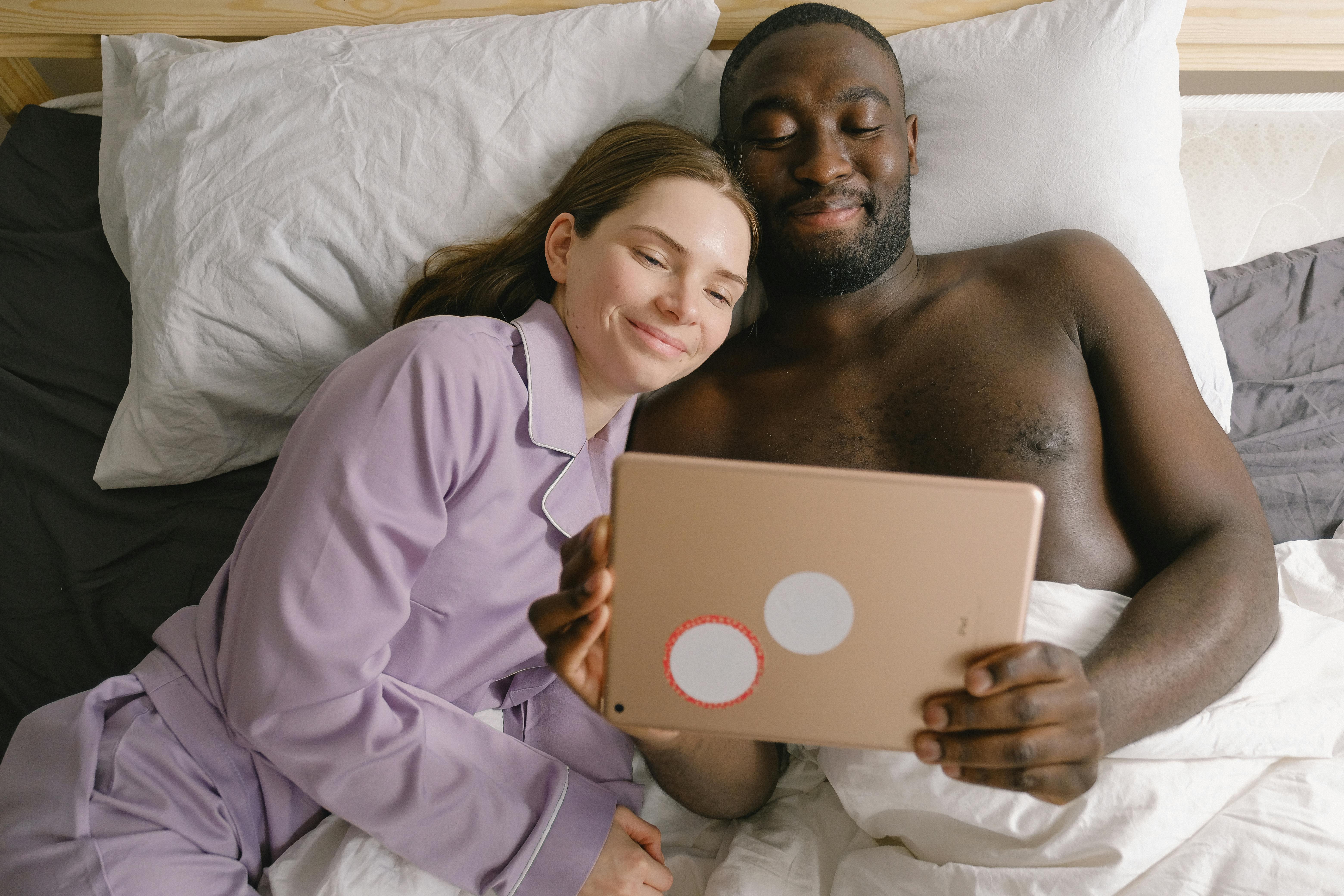 Smiling couple enjoying time together in bed, browsing on a tablet.