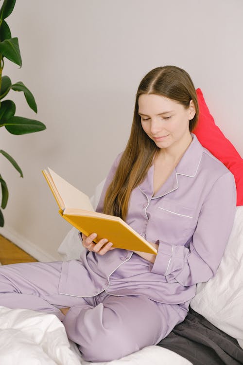 Free Content female in sleepwear with opened notepad in hands sitting on comfortable bed with cushions in light bedroom at home Stock Photo