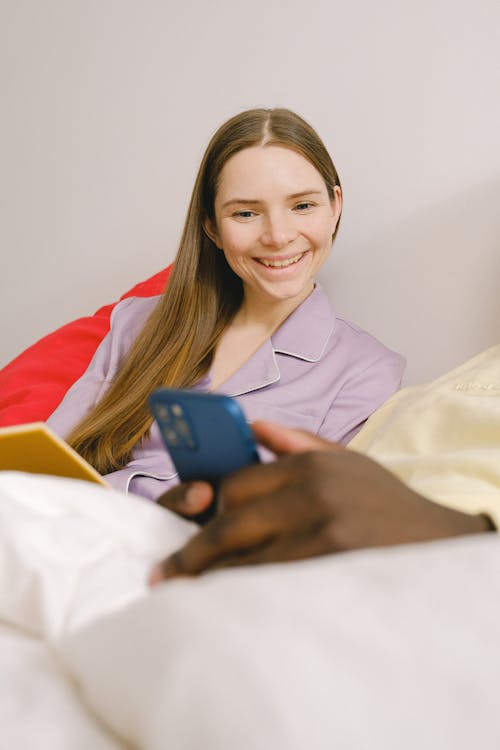 Free Happy woman looking at smartphone of unrecognizable black boyfriend on bed Stock Photo