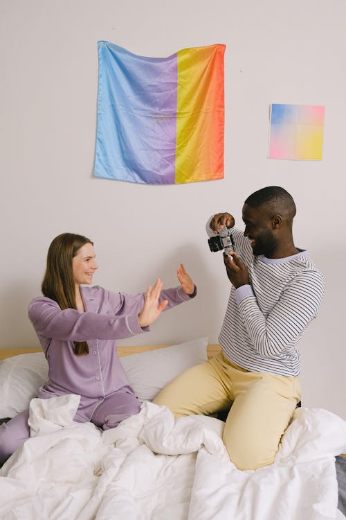 Cheerful black man taking photo of girlfriend in bedroom